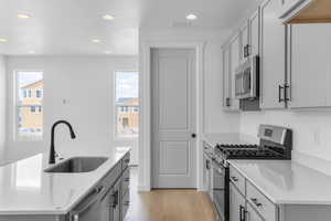 Kitchen with stainless steel appliances, recessed lighting, light wood-style floors, light countertops, and a center island with sink