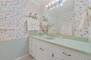 Bathroom featuring wallpapered walls, ornamental molding, and vanity