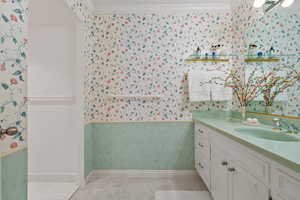 Bathroom featuring wallpapered walls, vanity, and ornamental molding