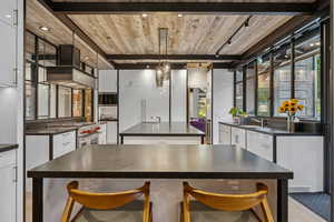 Kitchen with dark countertops, high end stainless steel range oven, a wooden ceiling with exposed beams, and a kitchen island with sink