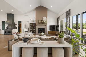 Living room with high vaulted ceiling, a large fireplace, wood finished floors, and recessed lighting