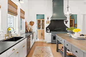 Kitchen with stainless steel appliances, custom range hood, dark countertops, light wood finished floors, and hanging light fixtures