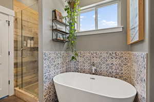 Full bathroom with a shower stall, a freestanding tub, tile walls, and a wainscoted wall
