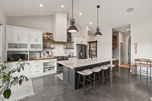 Kitchen with high quality appliances, open shelves, concrete floors, high vaulted ceiling, and white cabinets