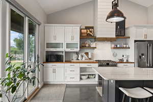 Kitchen with stainless steel appliances, open shelves, vaulted ceiling, backsplash, and white cabinets