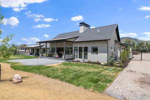 Back of property featuring stucco siding, a patio area, a shingled roof, a chimney, and a mountain view