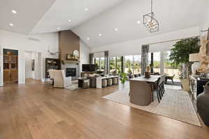 Dining area with high vaulted ceiling, a glass covered fireplace, light wood-style flooring, a chandelier, and recessed lighting