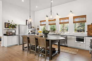 Kitchen featuring stainless steel appliances, dark countertops, light wood finished floors, recessed lighting, and a towering ceiling