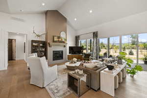 Living room with high vaulted ceiling, a glass covered fireplace, hardwood / wood-style floors, and recessed lighting