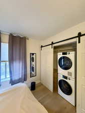 Laundry room with stacked washer / drying machine, a barn door, and light wood finished floors