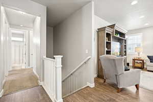Corridor featuring an upstairs landing, wood finished floors, and recessed lighting