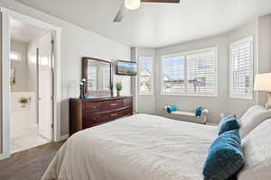 Carpeted bedroom featuring multiple windows, ensuite bath, and a ceiling fan