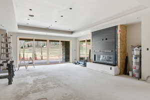 Unfurnished living room with unfinished concrete flooring, a raised ceiling, and a glass covered fireplace