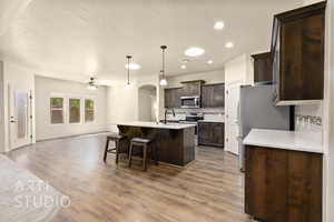 Kitchen with stainless steel appliances, open floor plan, dark brown cabinetry, decorative backsplash, and ceiling fan