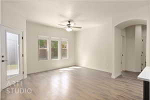 Unfurnished living room with arched walkways, ceiling fan, wood finished floors, and healthy amount of natural light
