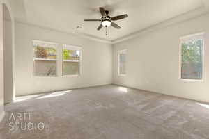 Carpeted spare room featuring a raised ceiling, a ceiling fan, and arched walkways