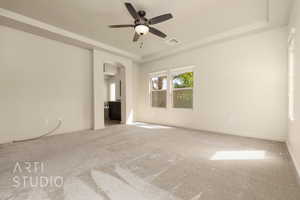 Carpeted empty room featuring a raised ceiling, arched walkways, and ceiling fan