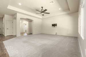 Unfurnished room featuring a tray ceiling, a ceiling fan, arched walkways, light colored carpet, and recessed lighting