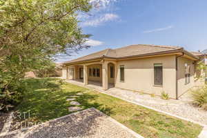 Rear view of property with stucco siding, a yard, a patio, and a tiled roof