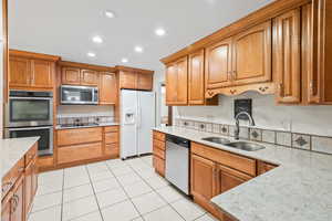Kitchen with stainless steel appliances, light stone counters, recessed lighting, brown cabinets, and light tile patterned floors