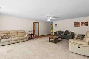 Living area with light carpet, a ceiling fan, and ornamental molding