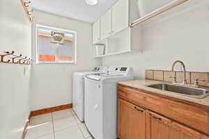 Laundry area with washing machine and clothes dryer, cabinet space, and light tile patterned floors