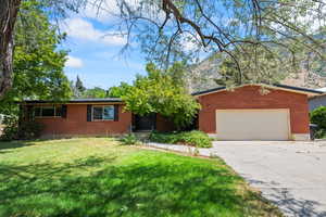 View of front facade featuring brick siding, driveway, a front lawn, a garage, and a mountain view