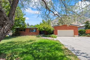 Ranch-style house featuring driveway, a front lawn, an attached garage, and brick siding