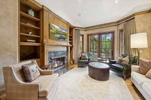 Living room featuring vaulted ceiling, a high end fireplace, built in shelves, and wood finished floors