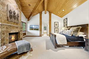 Carpeted bedroom featuring a wooden ceiling with exposed beams, a fireplace, and high vaulted ceiling