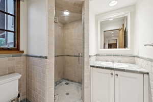 Full bath with tile walls, vanity, a stall shower, recessed lighting, and wainscoting