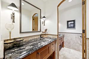Bathroom featuring vanity, a wainscoted wall, tile walls, and stone finish flooring
