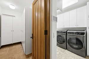 Laundry room with stone tile flooring, independent washer and dryer, and cabinet space