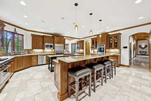 Kitchen featuring stainless steel appliances, stone tile flooring, a large island, brown cabinetry, and crown molding