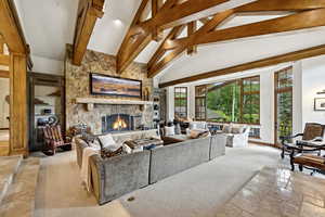 Living room with a stone fireplace, stone tile floors, beamed ceiling, and high vaulted ceiling