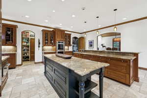 Kitchen featuring arched walkways, a large island with sink, stone tile floors, stainless steel double oven, and brown cabinets