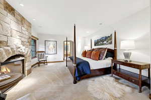 Bedroom with light colored carpet, a stone fireplace, and recessed lighting