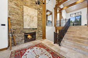 Entrance foyer featuring stairway, a stone fireplace, a chandelier, stone tile flooring, and beam ceiling