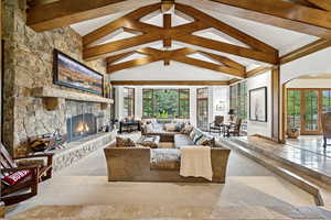 Living room featuring a stone fireplace, beam ceiling, high vaulted ceiling, and arched walkways