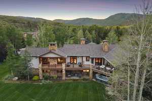 Rear view of property with a chimney, stone siding, a yard, a deck with mountain view, and stucco siding