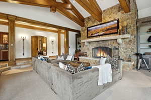 Carpeted living area with arched walkways, a stone fireplace, beam ceiling, and high vaulted ceiling