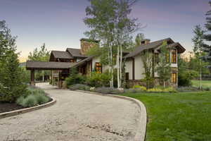 View of front of property featuring stone siding, a chimney, a front lawn, and concrete driveway