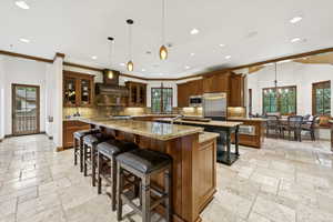 Kitchen featuring wall chimney exhaust hood, a large island with sink, stainless steel appliances, stone tile flooring, and recessed lighting
