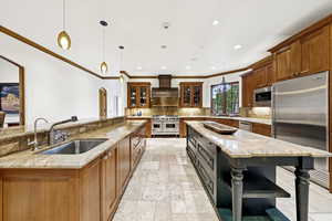 Kitchen with high quality appliances, custom exhaust hood, a large island, stone tile floors, and ornamental molding