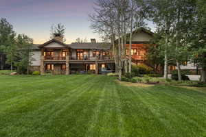 Back of property at dusk featuring stone siding, a yard, a chimney, a wooden deck, and stairs