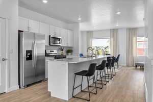Kitchen featuring stainless steel appliances, a breakfast bar area, an island with sink, light wood-style floors, and white cabinets