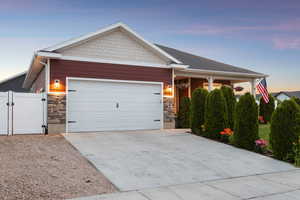 Craftsman house with stone siding, an attached garage, concrete driveway, and a gate