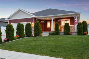 Craftsman-style house with stone siding, a garage, a porch, and a yard