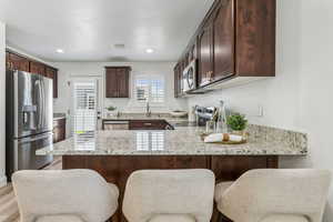 Kitchen with stainless steel appliances, a peninsula, dark brown cabinets, light stone counters, and light wood-style flooring