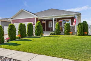 View of front of house featuring a garage, covered porch, a front lawn, and stone siding